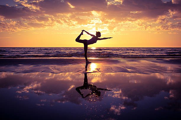 silhouette of woman practicing yoga on the beach at sunset