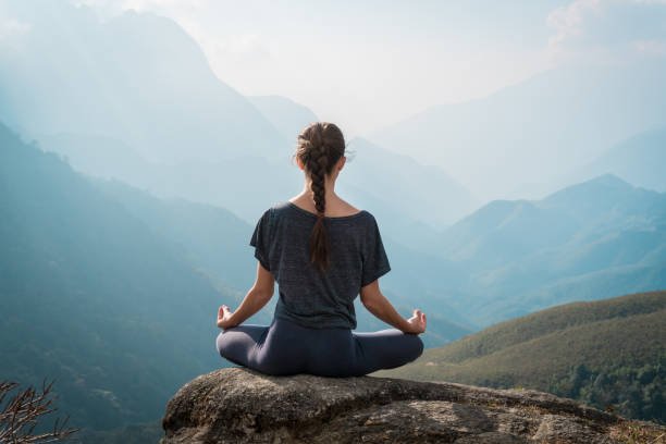 woman meditates in yoga asana padmasana lotus pose on mountain cliff