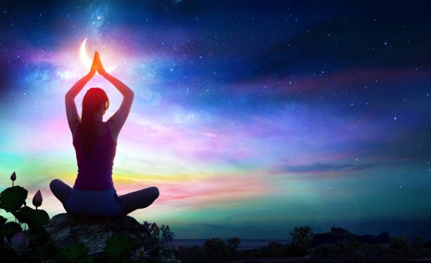 woman doing yoga with lotus flowers and rainbow gradient in the sky at night